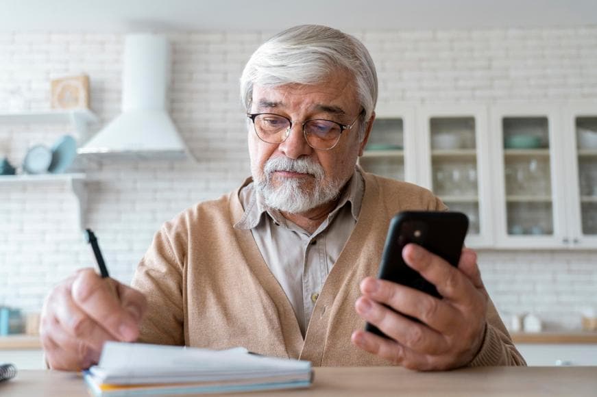 Close up of senior person writing and holding a phone with the other hand