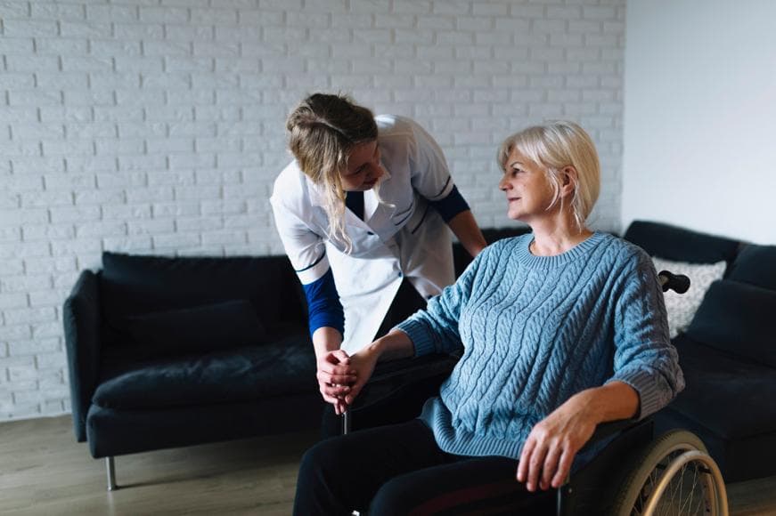 Senior woman in wheelchair with registered nurse to the side holding her hand