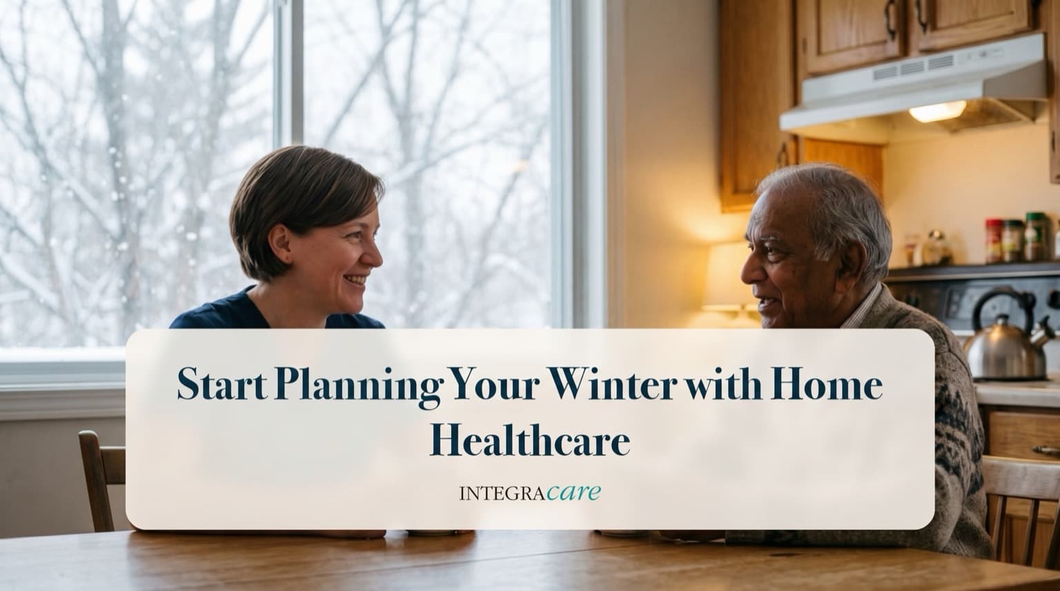 A caregiver and a senior man chatting over tea at a kitchen table beside a large window with snow falling outside