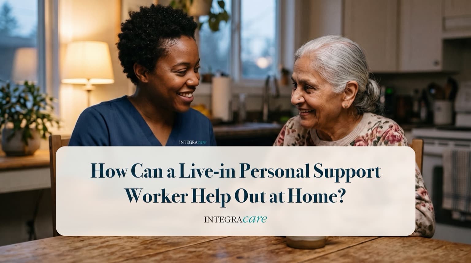 Personal support worker in navy scrubs and a senior woman smiling at each other over tea at a kitchen table