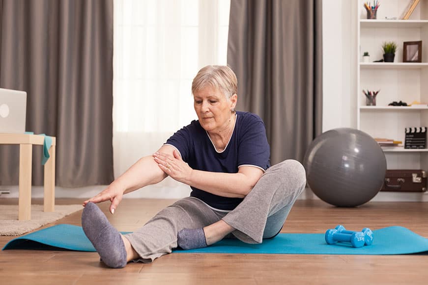 active Senior stretching her leg on a yoga mat