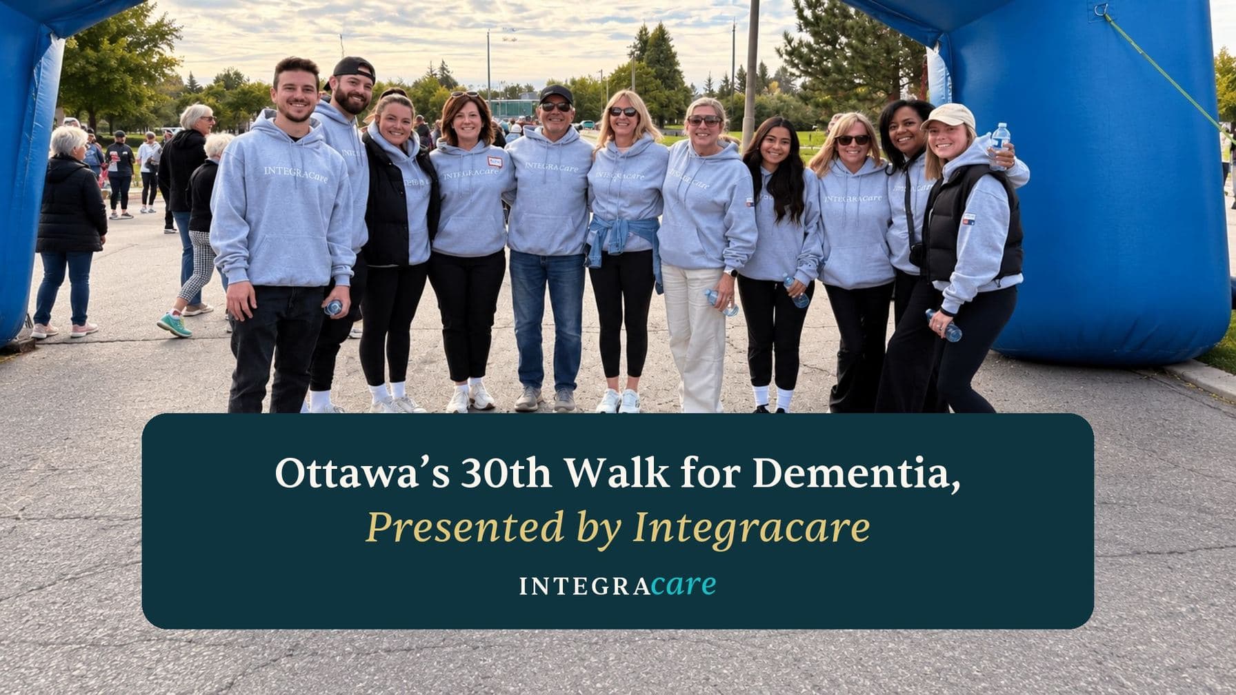 The Integracare team in matching grey Integracare hoodies at the start arch of Ottawa's 30th Walk for Dementia, beside the title Ottawa’s 30th Walk for Dementia, Presented by Integracare.