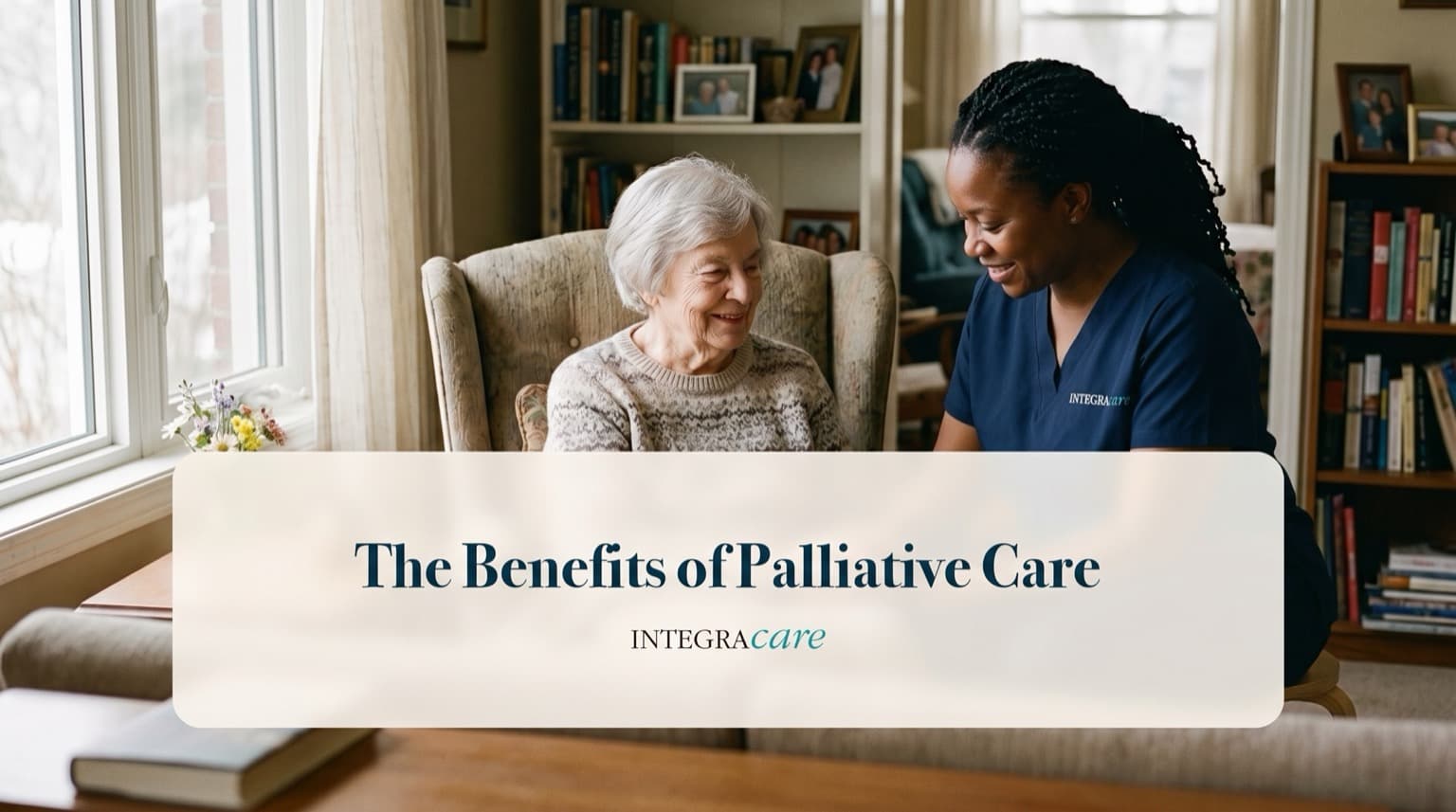Caregiver sitting beside a senior woman in an armchair as they chat in her book-lined living room