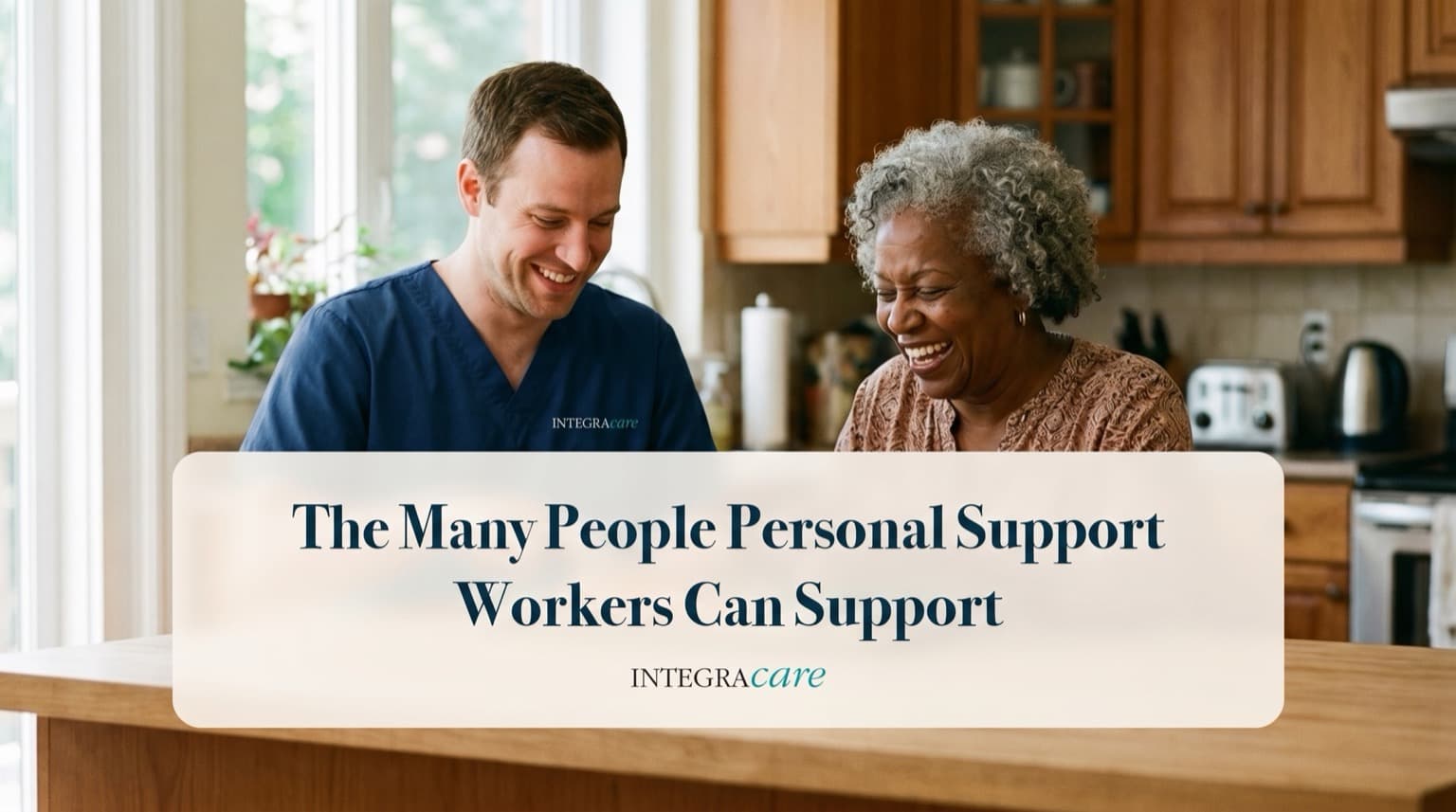 Smiling caregiver in navy scrubs sharing a laugh with an older woman at the counter of a bright home kitchen