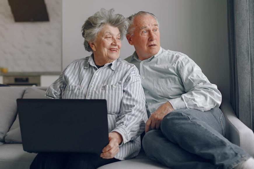 Senior couple sitting on sofa at home using a laptop