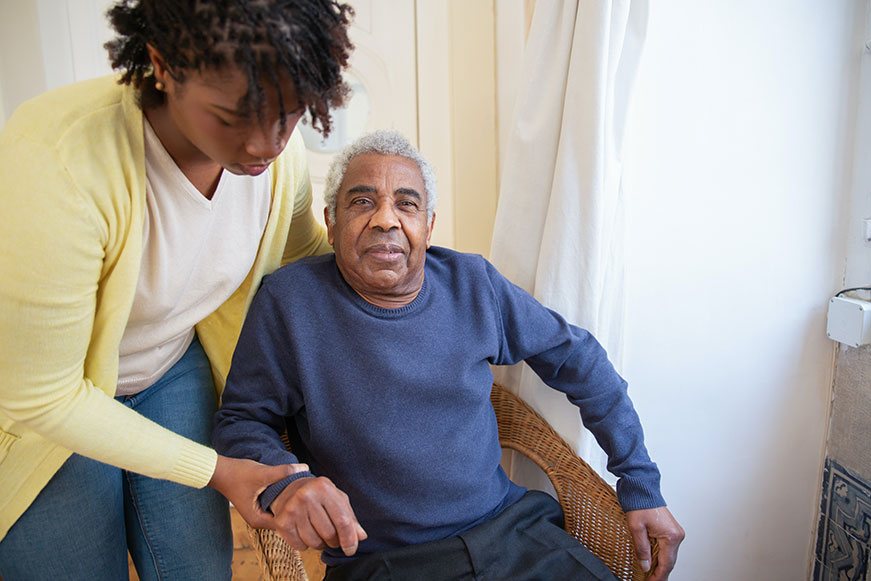 A caregiver helping an older man sit down in a chair