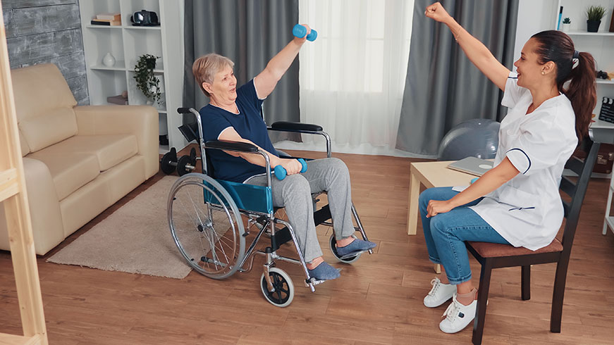Senior woman sitting in a wheelchair lifting weights doing exercises with a Physiotherapist