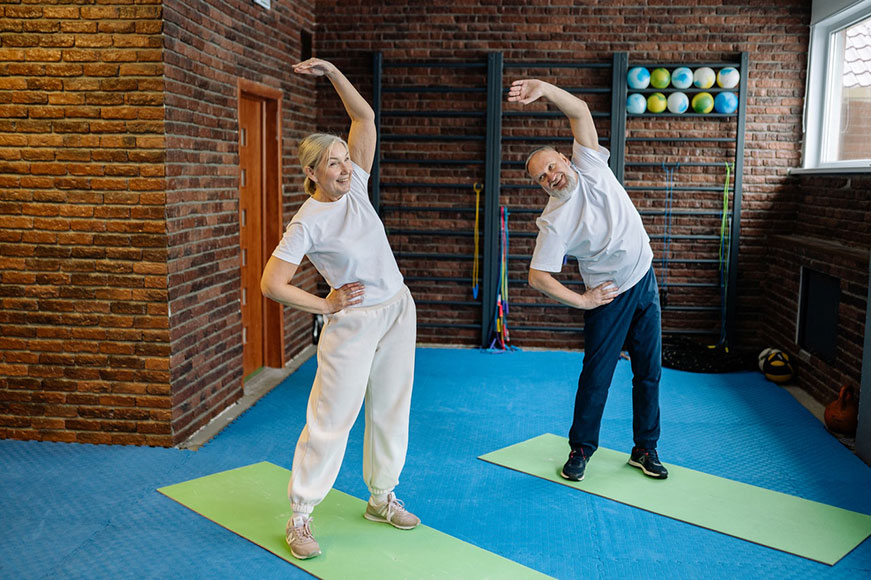 Senior woman and man stretching their arms overhead in a gym