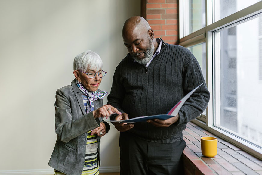 Two people are looking through a book. The senior lady is pointing at a page