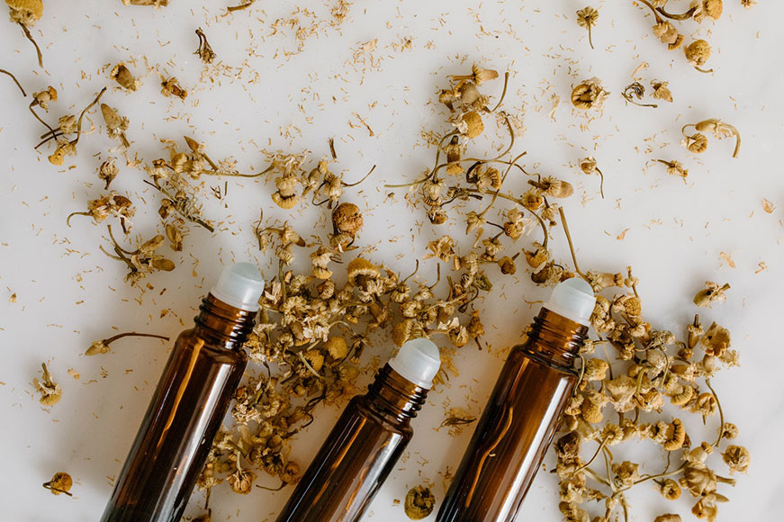 An up-close shot of three brown essential oil roller bottles on a white table with dried flowers scattered around them.