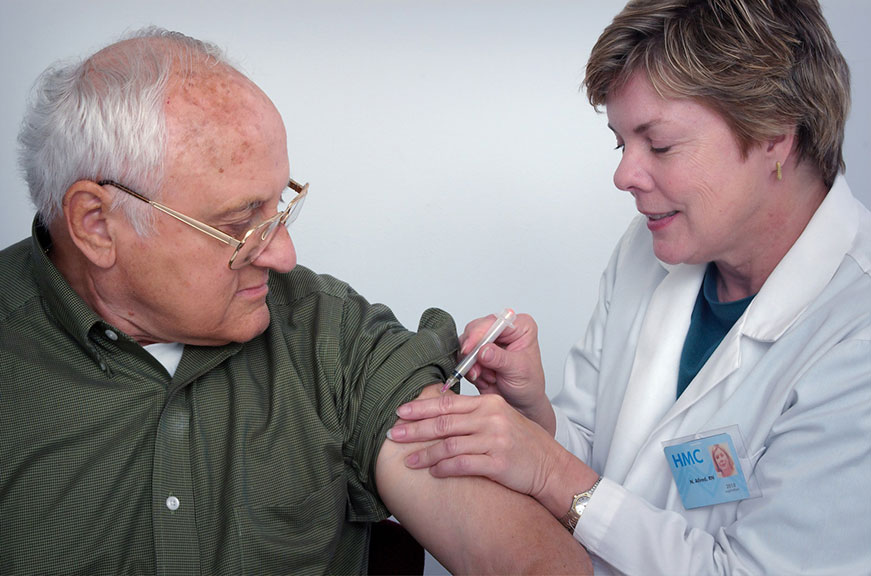 A senior man up close getting a shot in the arm from a healthcare practitioner