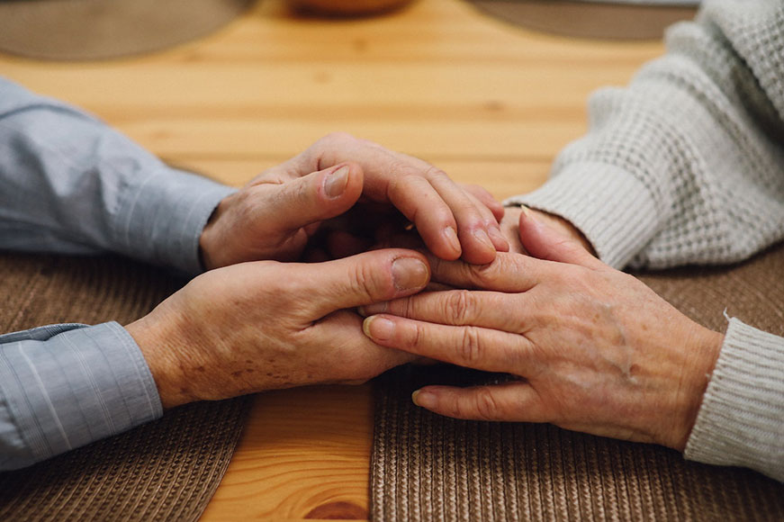 An up-close photo of seniors holding hands atop a wooden table