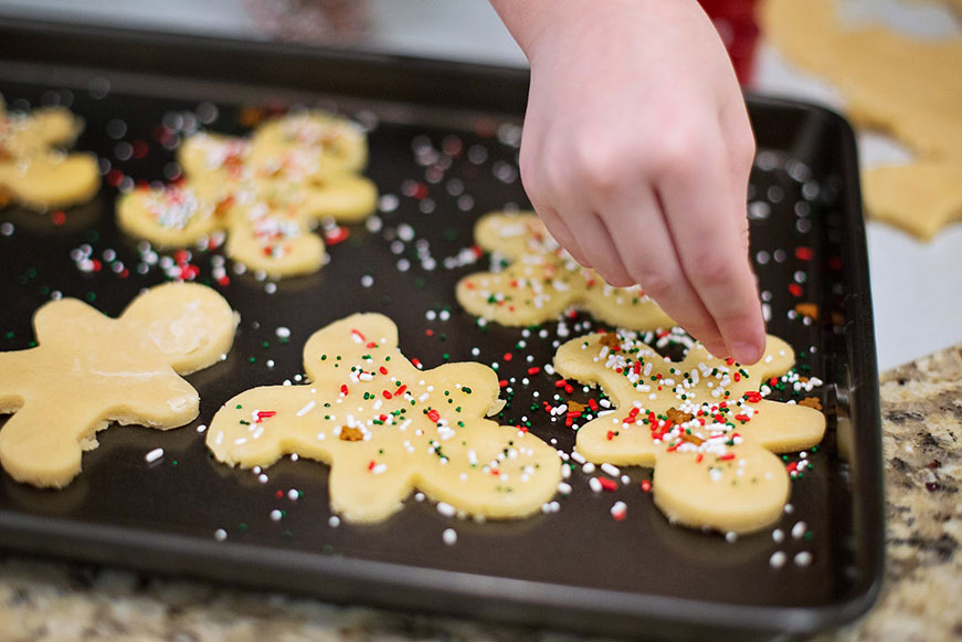 A close-up photo of someone putting sprinkles on holiday cookies
