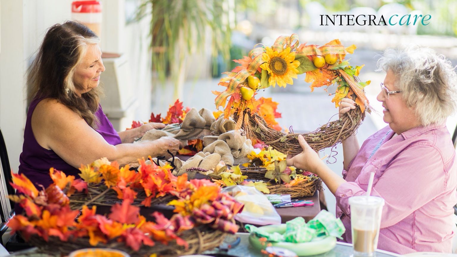 Two senior women creating fall wreaths together at a table, promoting engaging activities and companionship – Integracare.