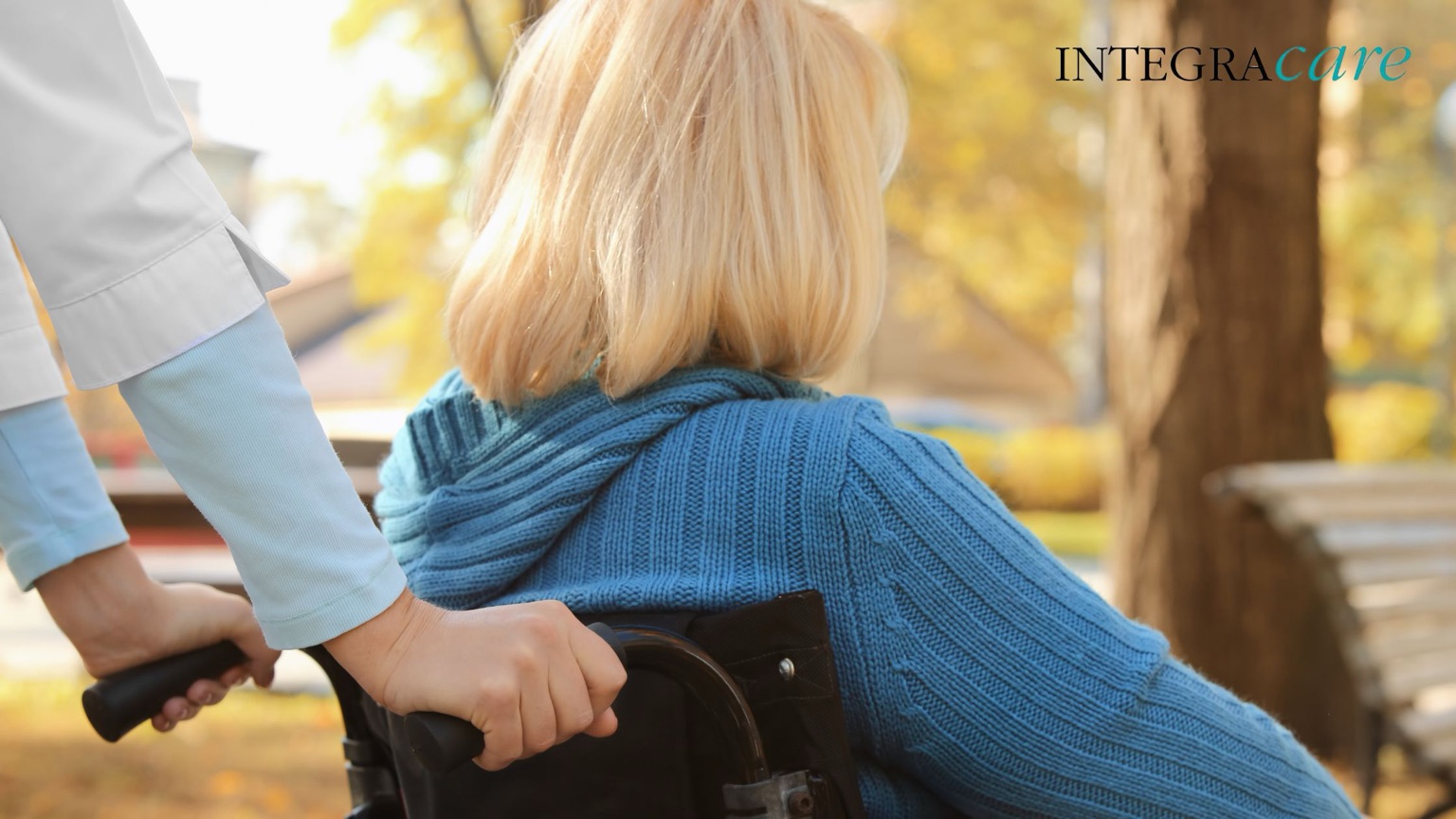 Caregiver pushing an elderly woman in a wheelchair through a park in autumn, symbolizing Integracare’s compassionate senior home health care.