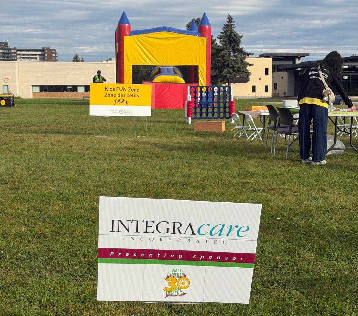 An Integracare presenting sponsor lawn sign in the grass beside the Kids Fun Zone and a bouncy castle at Ottawa's 30th Walk for Dementia.