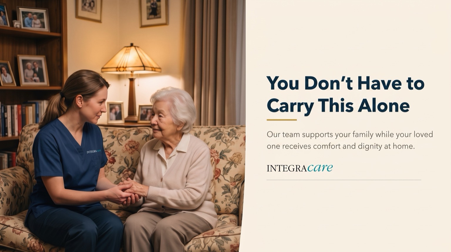 A caregiver holds a senior woman's hands as they talk together on a floral sofa